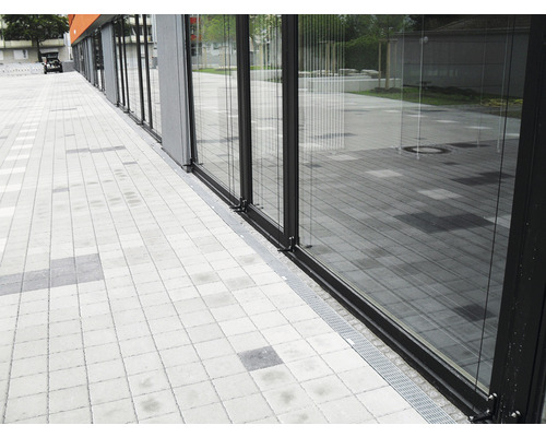 Glasfassade mit Entwässerungsrinne vor gepflastertem Gehweg