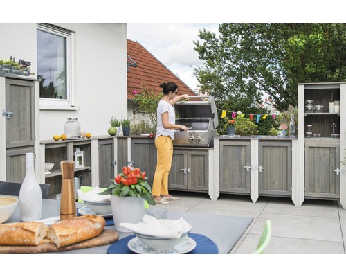 Outdoor-Küche mit Grill, Schränken und Zubereitungsbereich auf einer Terrasse, während eine Frau grilliert