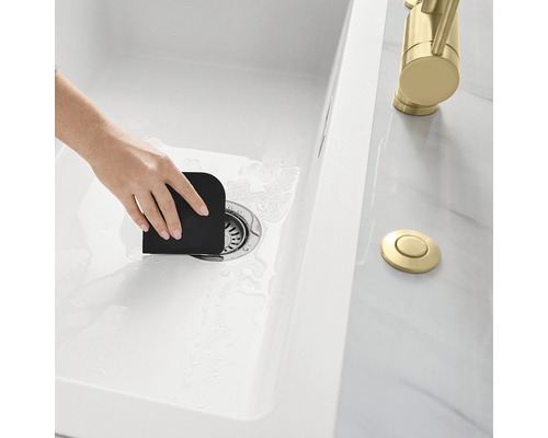 Eine Person benutzt einen Spatel in einem Spülbecken, um Essensreste zu entfernen.