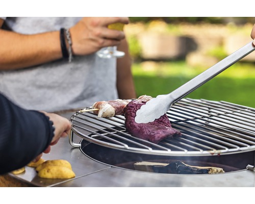 Fleisch wird mit einer Grillzange auf einem Grill zubereitet.