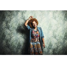 Frau mit gemustertem Kleid vor einer Wand mit Palmenblattmuster