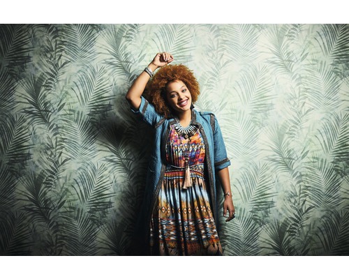 Frau mit gemustertem Kleid vor einer Wand mit Palmenblattmuster