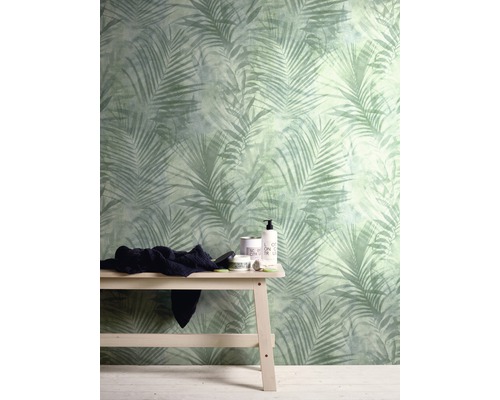Raum mit einer Wandtapete mit Palmenmuster und einer Holzbank mit Textilien und Badutensilien.