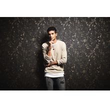 Mann mit Pullover vor einer gemusterten Wand