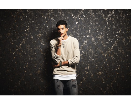 Mann mit Pullover vor einer gemusterten Wand