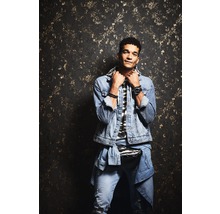 Mann mit Jeansjacke und Jeans vor gemusterter Wand