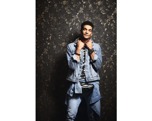 Mann mit Jeansjacke und Jeans vor gemusterter Wand