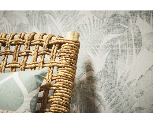 Detailansicht eines Rattanmöbels vor einer Wandtapete mit Blattmuster