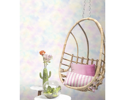 Scène avec fauteuil suspendu en rotin, coussins et décoration sur une table d''appoint.