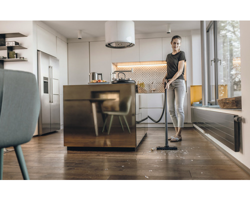 Femme aspire des éclats dans une cuisine moderne avec un aspirateur