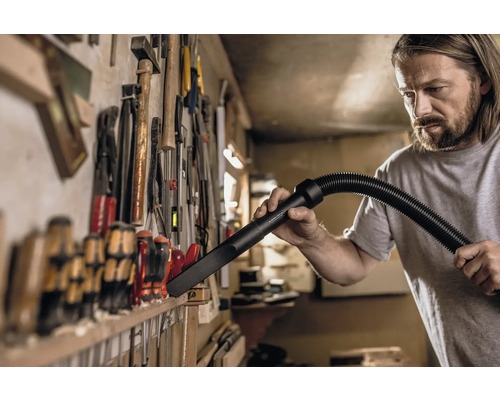 Un homme nettoie un mur à outils avec un aspirateur