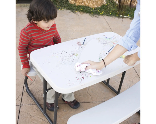 Un enfant peint à table et une personne essuie la surface