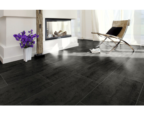 Salon avec carrelage foncé, cheminée et fauteuil.