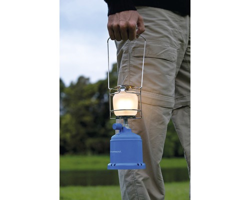 Une personne tient une lampe Camping Gaz avec une poignée en métal.