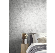 Chambre avec papier peint gris imitation béton, lit et table d''appoint en bois.