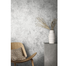 Scène avec chaise en bois, coussin, vase et branches décoratives devant un mur gris