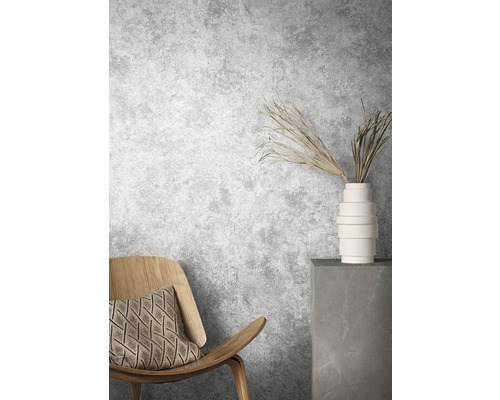 Scène avec chaise en bois, coussin, vase et branches décoratives devant un mur gris