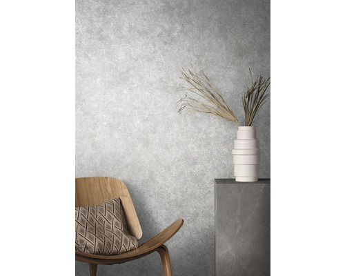 Intérieur décoratif avec chaise, coussin, vase et plantes ornementales devant un mur texturé