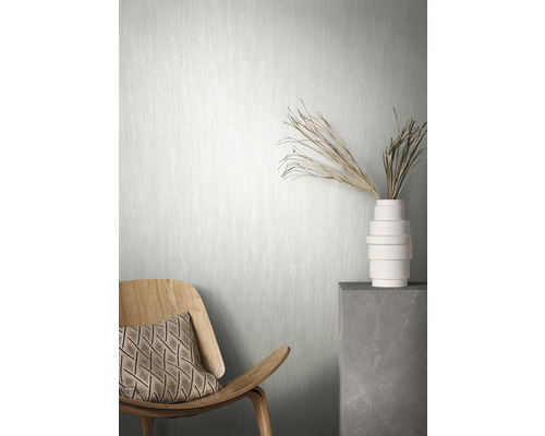 Scène avec un papier peint intissé clair, une chaise en bois avec coussin et un vase avec décoration sur un socle