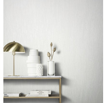 Nature morte décorative avec lampe de table, vases et livres devant un papier peint structuré