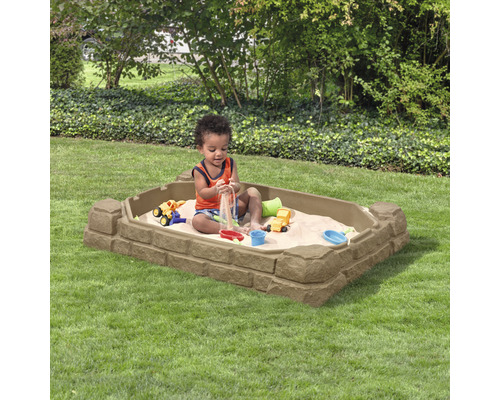 Un jeune enfant joue dans un bac à sable rectangulaire à motif de pierre dans le jardin.