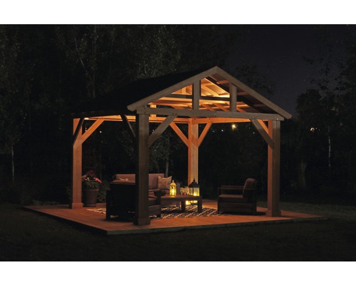 Beleuchteter Pavillon mit Gartenmöbeln auf Holzterrasse bei Nacht.