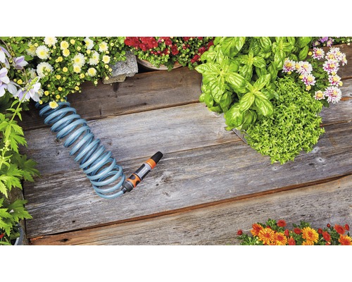 Scène de jardin avec tuyau spiralé, fleurs et herbes aromatiques sur plancher en bois