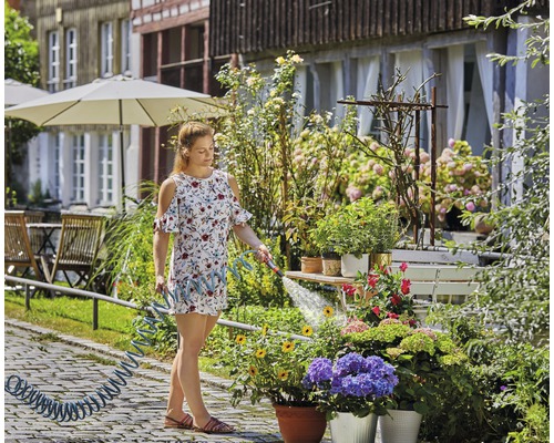 Femme arrose des fleurs avec un tuyau d''arrosage dans le jardin.