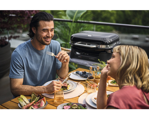 Paar isst Gegrilltes am Tisch mit Elektrogrill im Hintergrund