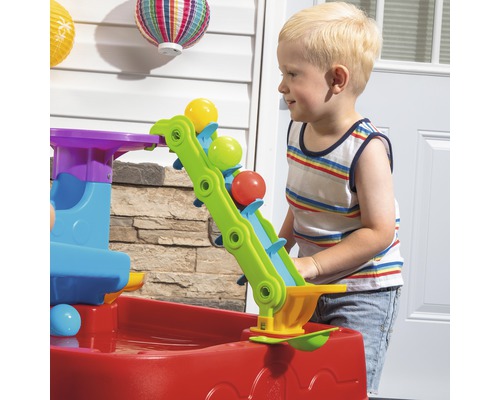Un enfant joue avec une table d''eau colorée avec des balles dans le jardin.