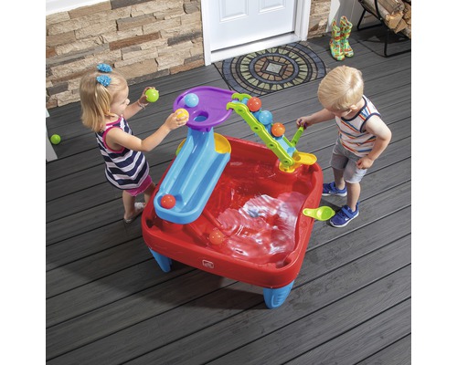 Deux enfants jouent avec une table d''eau Step2 à l''extérieur avec des toboggans et des balles.