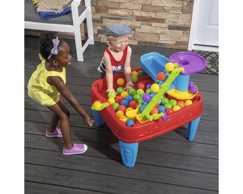 Des enfants jouent avec une table de jeu avec des balles dans le jardin.