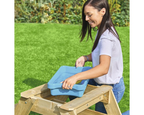 Femme remplissant un récipient d''eau bleu sur une table de pique-nique dans le jardin