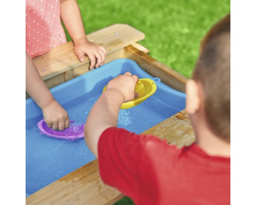 Des enfants jouent avec des bateaux jouets dans l''eau sur une table à sable et à eau en bois.