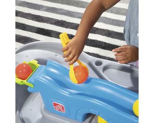 Un enfant joue avec une table de jeu Step2 et utilise une pince pour attraper des balles