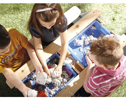 Trois enfants jouent avec du sable sur une table à sable à l''extérieur.