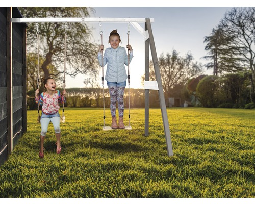 Deux enfants se balancent sur une balançoire en bois dans le jardin.