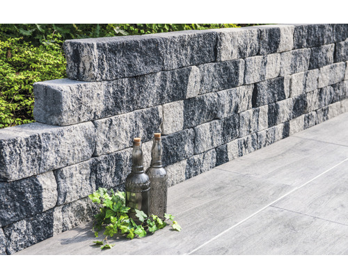Stützmauer aus Betonsteinen mit dekorativen Flaschen und Pflanzen auf Bodenplatten