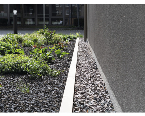 Bordure de parterre en pierre entre les plantes et le mur de la maison
