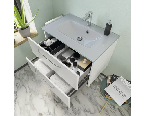 Meuble-lavabo blanc avec deux tiroirs ouverts, vasque à poser, robinetterie et divers articles de toilette