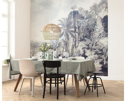 Salle à manger avec table, chaises, suspension en rotin et papier peint photo tropical.