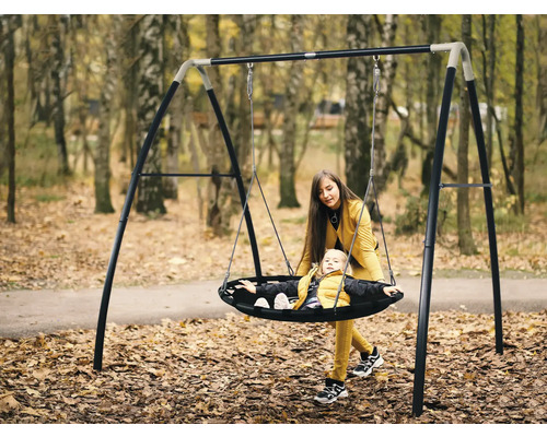 Mère poussant son enfant sur une balançoire nid d''oiseau avec cadre en acier dans le jardin
