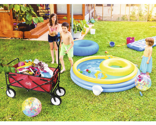 Szene im Garten mit Kindern, einem Bollerwagen mit Spielsachen und einem Planschbecken