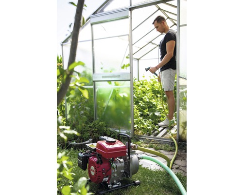 Motopompe de jardin en service devant une serre avec jardinier
