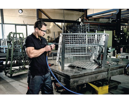 Un homme travaille avec une visseuse pneumatique sur une grille métallique dans un atelier.