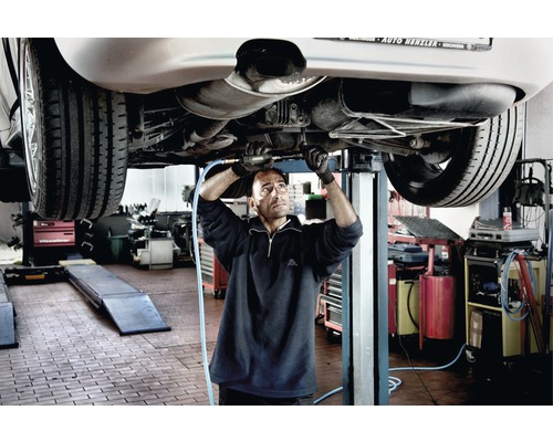 Ein Mechaniker arbeitet an einem Auto auf einer Hebebühne in einer Werkstatt.