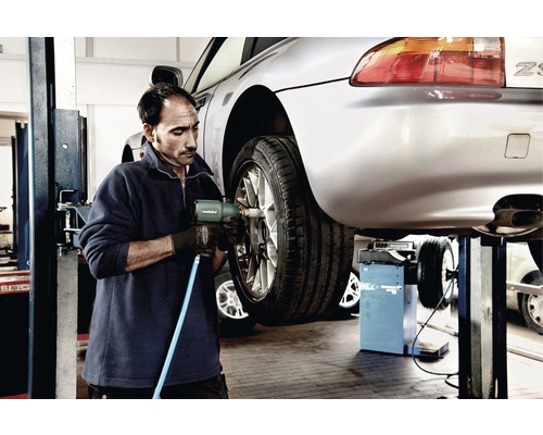 Ein Mechaniker wechselt mit einem Schlagschrauber ein Rad an einem Auto auf einer Hebebühne.