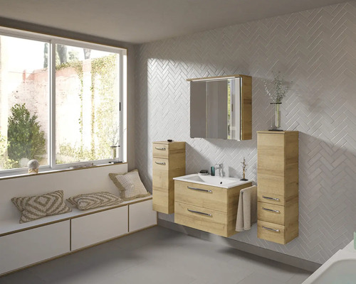 Badezimmer mit Waschtisch, Spiegelschrank und Hochschrank in hellem Holzdekor vor einer Wand mit Fischgrätenmuster.