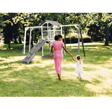 Aire de jeux avec balançoire, toboggan et cabane de jeux dans le jardin. Une femme tient la main d''un enfant.