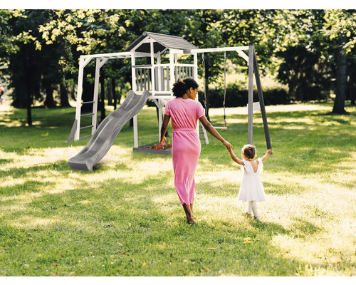 Spielplatz mit Schaukel, Rutsche und Spielhaus im Garten. Eine Frau hält die Hand eines Kindes.